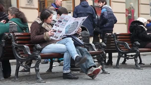 Lwów, Ukraina - 28 lutego 2015 dwóch turystów, mężczyzna i kobieta, studiując mapę zwiedzanie siedząc na ławce i jest otoczony przez męczącej codzienności — Wideo stockowe