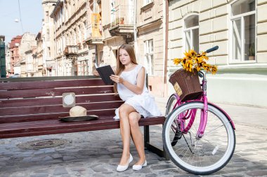 girl with bicycle sitting on bench and reading book clipart