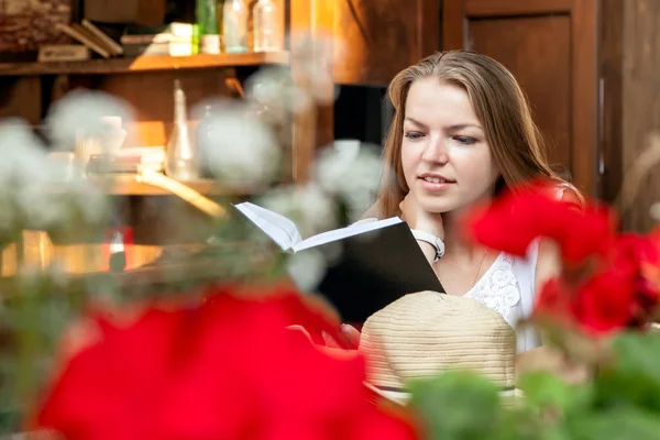 Smiling girl sitting at summer terrace and reading book — Stock Photo, Image