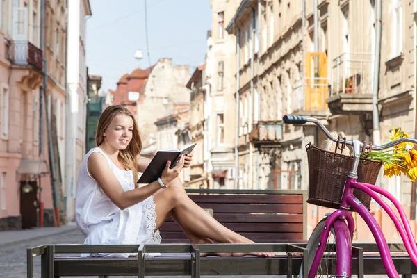 Chica con bicicleta sentado en el banco y libro de lectura —  Fotos de Stock