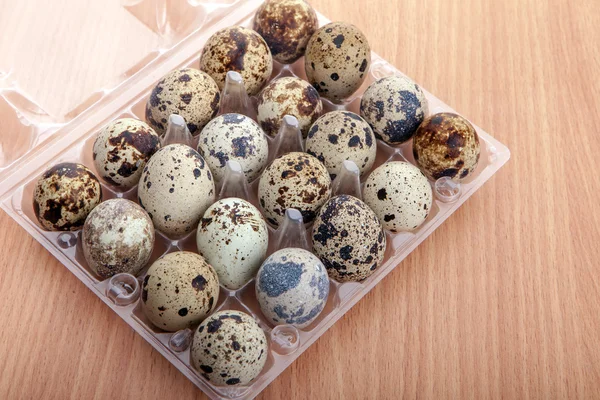 Ovos de codorna em recipiente plástico transparente na mesa de madeira — Fotografia de Stock