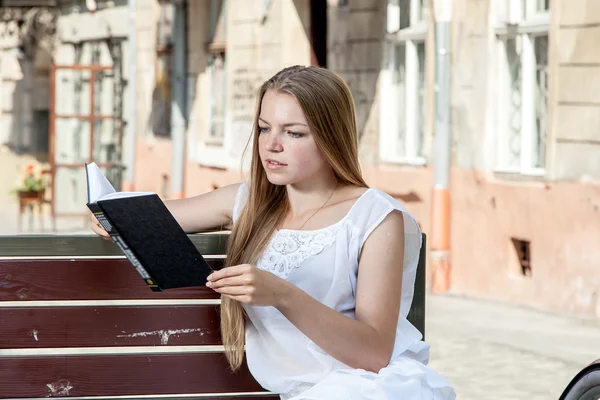 Meisje met fiets zittend op een bankje en lezen van boek — Stockfoto