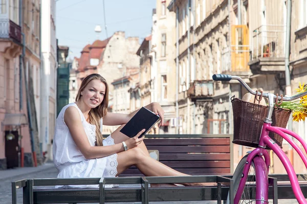 Meisje met fiets zittend op een bankje en lezen van boek — Stockfoto