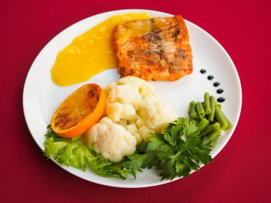 Kırmızı zemin üzerinde folyoda pişmiş somon balığı.