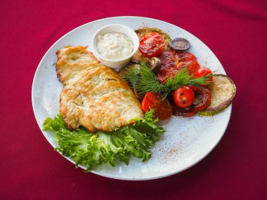 Kırmızı arka planda domatesli biftek ve otlar.