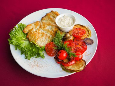 Kırmızı arka planda domatesli biftek ve otlar.