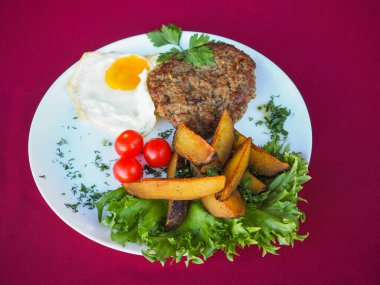 Kırmızı arka planda domatesli biftek ve otlar.