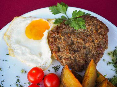 Kırmızı arka planda domatesli biftek ve otlar.