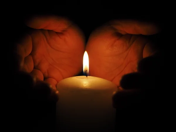 Candle and hands on a black background — Stock Photo, Image