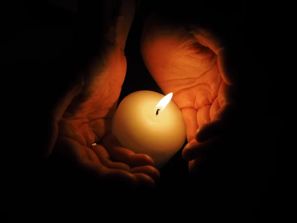 Candle and hands on a black background — Stock Photo, Image