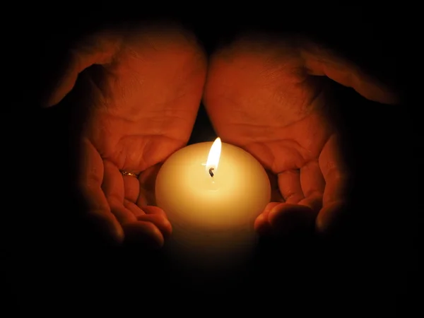 Candle and hands on a black background — Stock Photo, Image