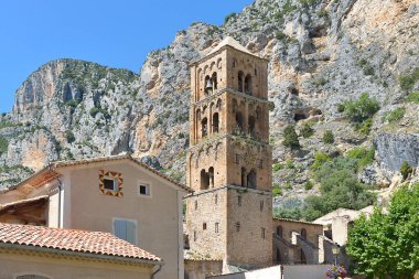 Moustiers-Sainte-Marie dağın eteklerinde ve Notre-Dame-de-l 'Assomption kilisesi kare çan kulesiyle. Moustiers-Sainte-Marie, Fransa 'nın güneydoğusunda yer alan Alpes-de-Haute-Provence bölgesinde bir komün.