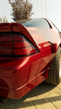 Düşük açılı, parlak kırmızı spor bir coupe 'un yakın plan çekimi, geniş arka lastiği vurguluyor, parlak spoiler, ve kare arka lamba tasarımı, dışarıda asfalt bir alanda sergileniyor.