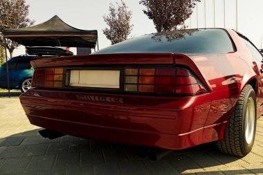 Parlak güneş ışığı altında bir açık hava sergisinde sergilenen, kare stop lambaları ve çift egzoz uçlarını vurgulayan, zengin bir kırmızı spor coupe 'un arka tarafındaki yakın çekim.