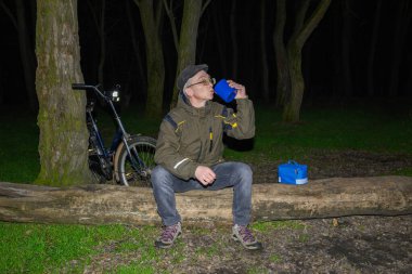 Susamış adam gece durağında mavi plastik bardaktan sıcak bir şeyler içiyor.