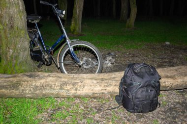Mavi yol bisikleti, gece ormanlarında eski ağaç gövdesine yaslanır. Turist sırt çantasının yanında dinlenme tesisinde düşmüş kütüklerin üzerinde yatar.