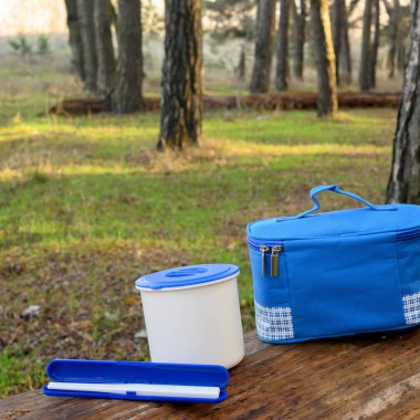 Mavi tekstil soğutucu çantası, beslenme çantası, ve sonbahar ormanındaki bir kütükte yemek çubukları için bir kutu, doğada Japon yemekleri için bir set.