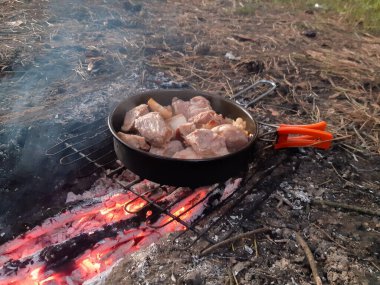 Et ve domuz yağı, yanan kömürlerin üzerinde metal bir ızgarada pişirilir, dumanla kaplanır, ormanda kuru çam iğneleri ve çimlerle çevrilir, dinlenme sırasında açık havada yiyecek izlerinin yakın çekimi yapılır.