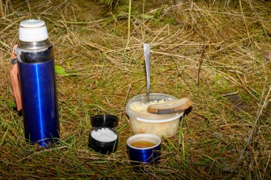 Orman zemininde açık bir termos, bir fincan çay, lahana turşusu ve dalların ve iğnelerin arasına tuz konmuş plastik bir kap var.