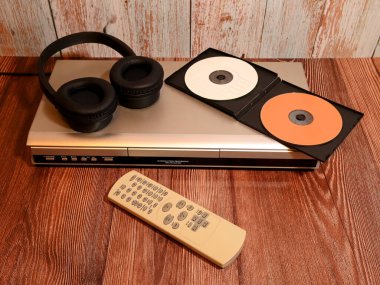 Üzerinde siyah kulaklıklar olan gümüş disk çalar ve tahta bir arka planda iki CD ile açık plastik bir çanta, uzaktan kumandalı bir ses sistemi