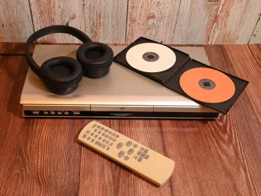 Tam boyutlu bir disk çalar, siyah kulaklıklar ve tahta bir yüzey üzerindeki uzaktan kumanda ünitesi de dahil olmak üzere ev içi multimedya ekipmanları.