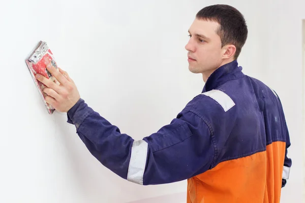 Handyman arbejder med sandpapir på en hvid væg . - Stock-foto