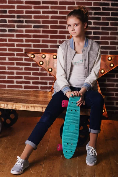 Hezká dospívající dívka s skateboard sedět ve studiu — Stock fotografie