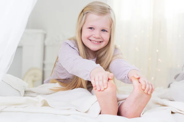 Glückliches Kindermädchen lächelt barfuß im Bett — Stockfoto