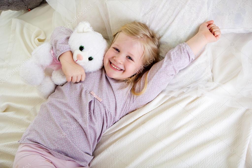 Child girl in the bed with white teddy bear