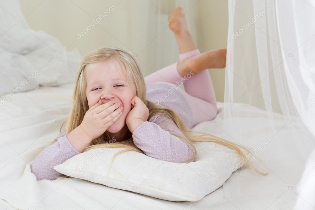 Tired cute child girl yawning in the bed