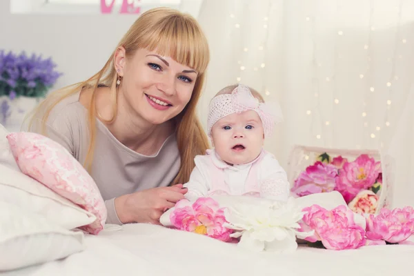 Mother and daughter are lying on bed with pink flowers — Stock Photo, Image