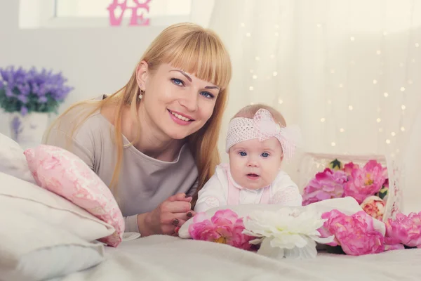 Mother and daughter are lying on bed with pink flowers — Stock Photo, Image