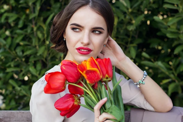 Mooie vrouw met tulpen zittend op de Bank — Stockfoto