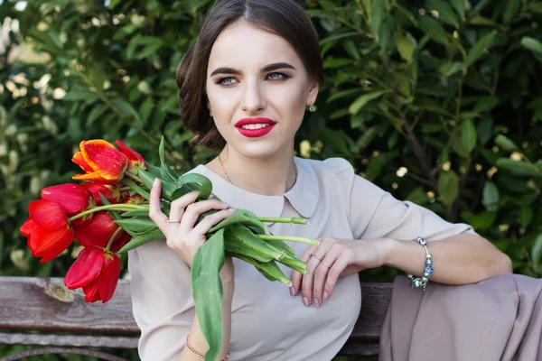 Mulher bonita com tulipas sentadas no banco — Fotografia de Stock