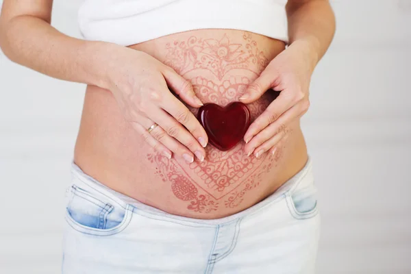 Red heart on pregnant belly with henna tattoo — Stock Photo, Image