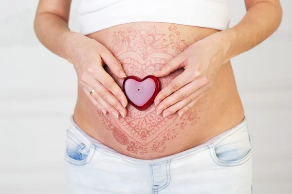 Red heart on pregnant belly with mehendi tattoo Stock Photo