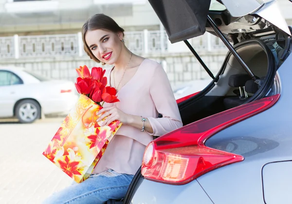Женщина с кучей тюльпанов возле машины — стоковое фото