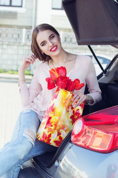 Woman with red tulips sitting in car trunk — Stock Photo, Image