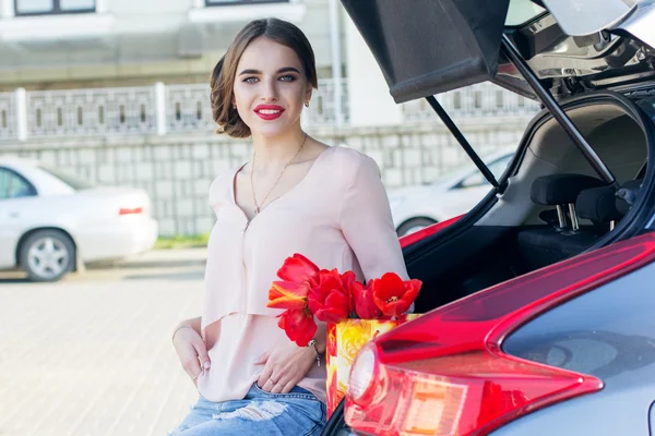 Mädchen mit roten Tulpen sitzt im Kofferraum — Stockfoto