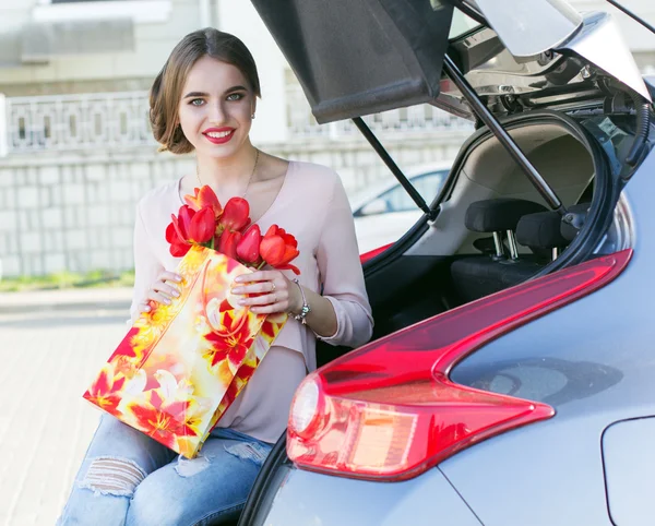 Meisje zit in de auto kofferbak met rode bloemen — Stockfoto