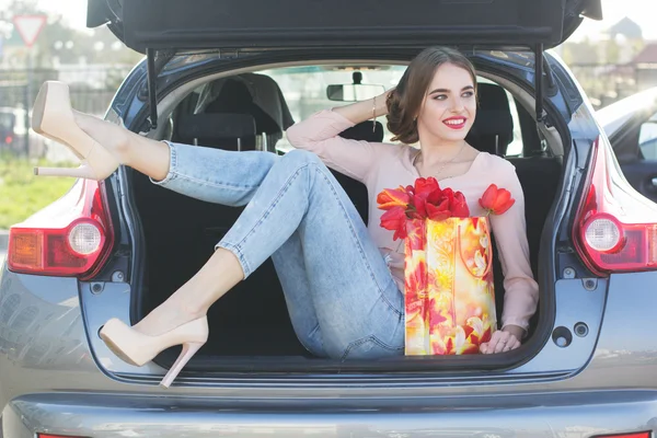 Menina está sentada no porta-malas do carro com pacote de presente — Fotografia de Stock
