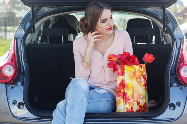 Девушка сидит в багажнике с подарочным пакетом — стоковое фото