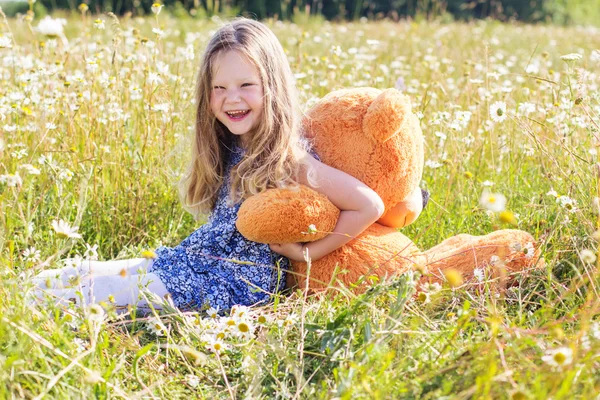 Dziecko dziewczynka w pole rumianek z misiem — Zdjęcie stockowe