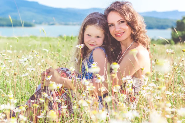 Mother and daughter are sitting in chamomile field — Stock Photo, Image