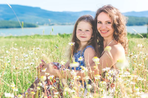 Mor och dotter sitter i kamomill fält — Stockfoto