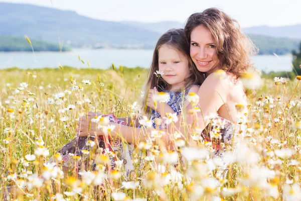 Mom and child girl are sitting in chamomile field — Stock Photo, Image