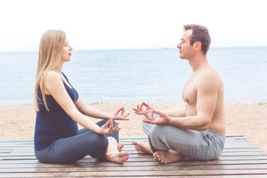 Hamile kadın ve erkek kumsalda yoga yapıyorsun