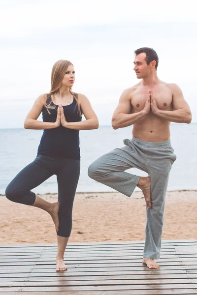Hombre y chica embarazada están haciendo yoga en la playa — Foto de Stock