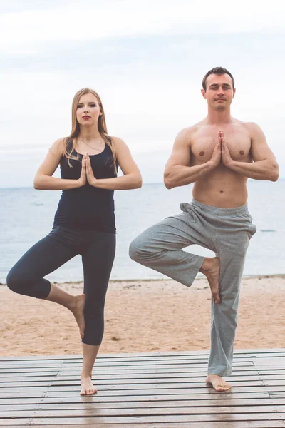 Hombre y chica embarazada están haciendo yoga en la playa —  Fotos de Stock