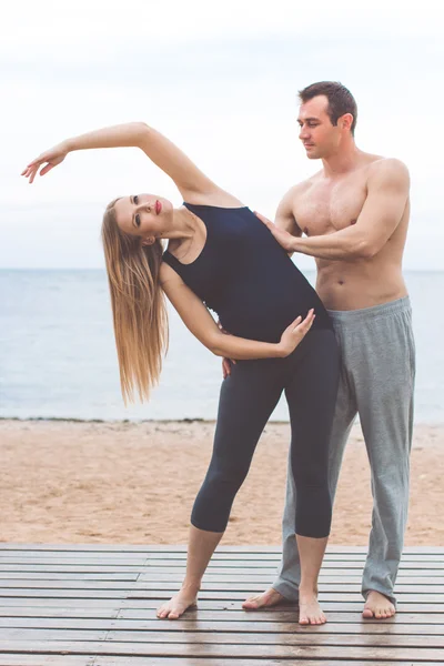 Man och gravid flicka gör yoga på stranden — Stockfoto